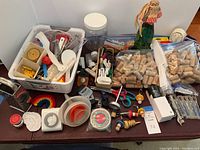 Wide view of assorted kitchen utility items including timers, scissors, funnels, corks, and utensils in small baskets and scattered on table.