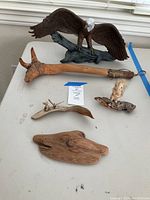Photo of a lot with a large dark brown bald eagle figure with white head and yellow beak on a base simulating tree branch, a light beige squirrel figure sitting on a piece of wood, small mouse family figurines on driftwood, three wooden carved decor pieces with natural texture and shapes, and a rustic wooden walking stick with a natural tree branch handle and leather wrap near the top.