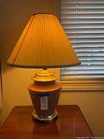 Mauve ceramic lamp with pleated shade on wooden surface near window