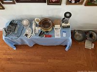 Full overview of all small kitchen appliances placed on a table with blue cloth, showing slicer, juicer, slow cooker, blender and food cutter, plus Farberware wok and base on the floor beside the table.