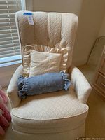 Front view of cream upholstered swivel rocker chair with two decorative throw pillows on the seat.