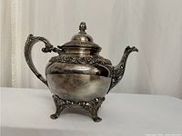 Side view of the silver plated coffee pot showing handle, spout, lid with finial, and decorative footed base.
