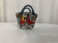 Front view of ceramic basket with cardinal birds and pinecone winter scene painted on it, blue handles visible.