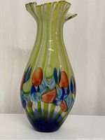 Front view of the extra large handblown glass vase showing green and white vertical stripes with colorful accents near the base.