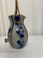 Side view of the glazed stoneware pitcher showing the blue floral decoration and bamboo handle attachment.