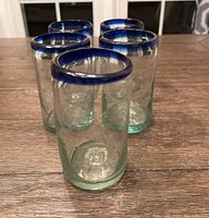 Front view of the 5 green-tinted handblown glasses with dark blue cobalt rim arranged on a wooden surface