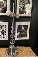 Full view lamp showing vertical glass ball column, chrome metal base, horizontal double bulb fixture, and pull chain switch.