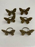 Six metal butterfly napkin holders arranged to show the butterfly faces and details