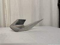 Photo of abstract metal sculpture on white background, showing side profile with flowing angular design and point.