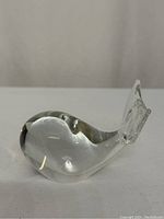 Side angle view of the clear glass whale paperweight showing the rounded body and upright tail fin.