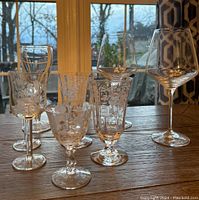 Six mixed antique and modern glasses including etched floral and geometric patterns and large modern wine glasses.