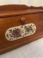 Front view of the wooden bread box showing fruit painted design on the front panel and wooden knob on the lid.