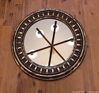 Full view of the round wall mirror showing the beveled glass and gold resin frame with oval detailing.