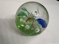 Clear spherical paperweight with green base, bubbles, and blue and red swirl