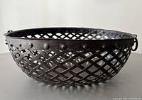 Front angled view of vintage wrought iron lattice fruit basket showing riveted band and ring detail on black background.