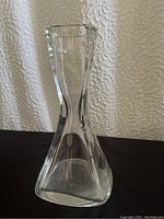 Front view of clear crystal bottle with angular, twisted design, showing wide base and narrow neck with square mouth.