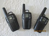 Three Uniden handheld radios with antennae placed on a white textured surface, showing front view and overall condition