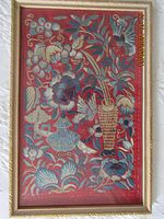 Full view of framed embroidery artwork showing entire piece with red background and colorful floral and bird designs.