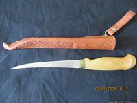 Fishing fillet knife fully sheathed in brown leather holder with visible embossed patterns and strap.