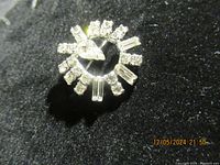 Front and angled views of the circular sterling silver brooch pin adorned with clear round and baguette rhinestones.