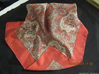 Angled photo showing the folded scarf with paisley pattern and burnt orange border.