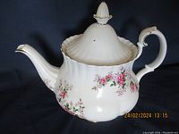Side view of white ceramic teapot with pink and lavender rose floral pattern and gold trim.