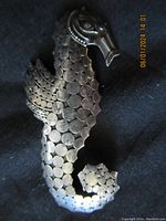 Close-up of the silver seahorse brooch showing scale texture and facial details.