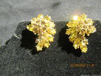 Pair of yellow gold-tone Trifari earrings with yellow and clear rhinestones viewed from top angle on black fabric background.