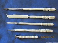 Top-down view of five vintage writing desk implements with carved bone handles on a dark blue fabric background.