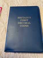 Blue leatherette case with gold embossed text 'Britain's First Decimal Coins'
