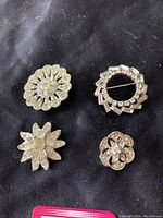 Set of four vintage rhinestone brooches displayed on black fabric, showing varying floral and geometric designs with silver-tone metal and clear rhinestones.