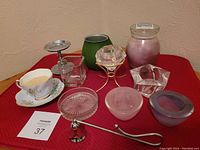 Photo of various glass, metal, and china candle holders and accessories arranged on a red surface.
