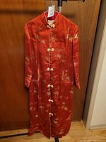 Front view of red ceremonial robe showing intricate gold embroidery, frog buttons and pockets with white trim