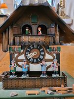 Front close-up of the chalet-style wooden cuckoo clock showing figurines and Roman numeral dial