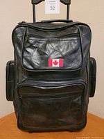 Front view of black leather rolling backpack showing Canadian flag patch and multiple zippered compartments.