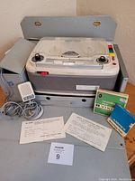 Geloso G-25 8A reel to reel recorder with microphone, carrying case, two tape boxes, and original documents laid out on floor