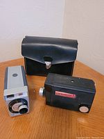 Two Kodak 8mm movie cameras with carrying case on wooden surface.