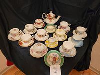 Overview of teapot centered behind 13 cups and saucers