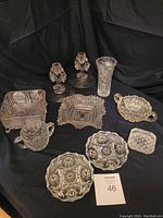 Full lot of vintage crystal and cut glass items including candle sticks, vase, candy dishes, and serving bowls arranged on black background.
