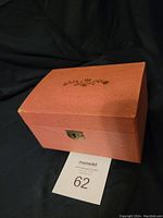 Closed rectangular pink textured music box with a gold floral design on lid and front lock.