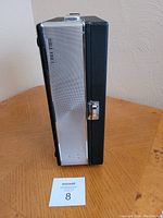 Side view of the Bible Voice reel to reel tape recorder in its closed metal and black case, showing latch and handle details.