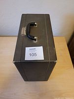 Closed black hard case with black handle and metal latch on table.