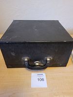 Black textured carrying case with metal latches and handle, closed view from the front.