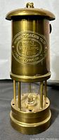 Front view of brass cylindrical lantern showing embossed plaque with manufacturer details.