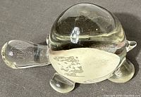 Clear glass turtle figurine shown from side angle on textured surface.
