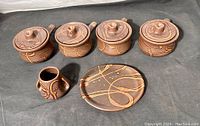 View of four covered French onion soup bowls, one small vase with two handles, and one round plate, all brown pottery with tan abstract drip decoration.