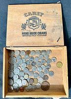 Top view of cedar cigar box containing the coin collection, showing branding inside lid and coins inside.
