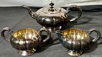 Photo showing the three-piece silver plated tea set with teapot, sugar bowl, and creamer, all with grooved rounded design and gold-toned interiors on sugar bowl and creamer.