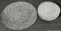 Photo showing one large serving plate and a stack of six smaller side plates, all clear glass with textured deep parallel grooves pattern.