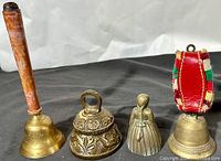 Four vintage brass and metal bells arranged side-by-side on a white backdrop, showing variety of size, shape and decoration.